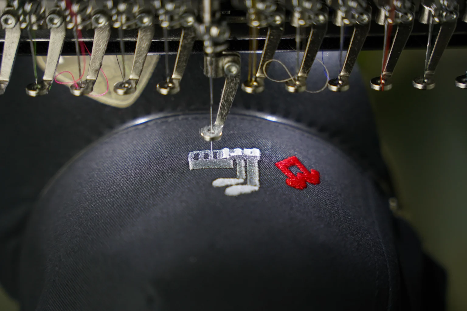 Nadelreihe der Stickmaschine über einer dunklen Cap